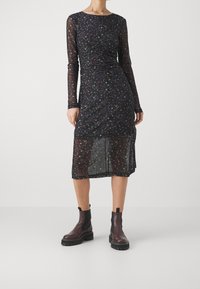 Mustat kukkakuosiset pitkähihaiset mekko, jossa on rypytetty yksityiskohta, läpikuultava rakenne ja polven pituinen helma, yhdistettynä tummiin nilkkabootseihin.