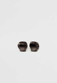 Sandalias deslizantes marrones con parte superior trenzada, suela plana y un acento de hebilla lateral. El material parece suave y flexible.