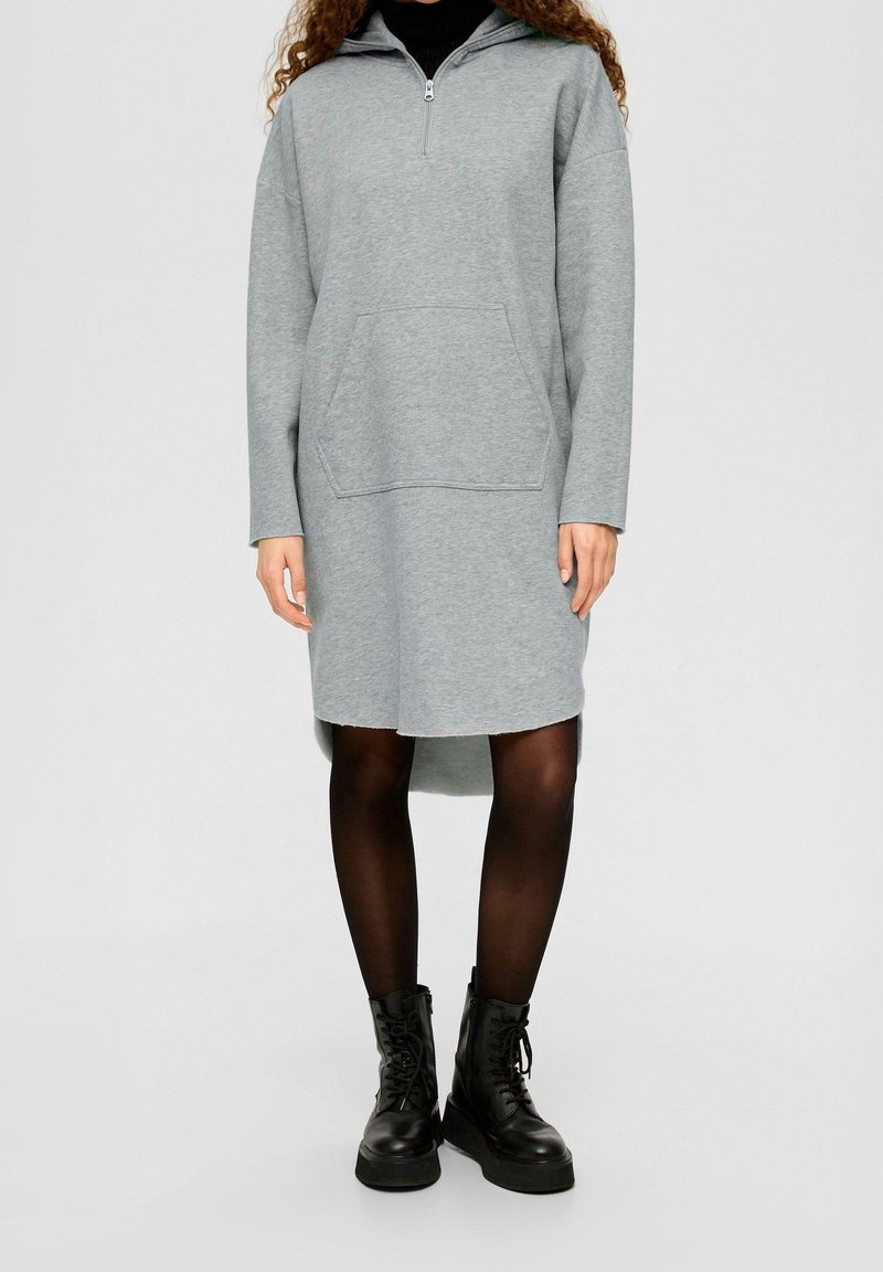 Šedé mikinové šaty s kapucí, s půlzipem vepředu, dlouhými rukávy a přední kapsou; doplněné o černé bojové boty a punčochy.