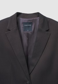 Blazer su misura marrone scuro con rever a punte, chiusura con un bottone e un'etichetta nera all'interno con scritto "CALLIOPE S".