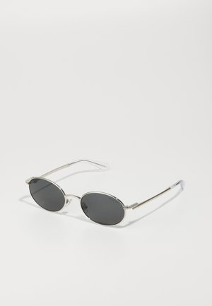 Ochelari de soare ovali cu lentile întunecate, cadran din metal argintiu, temple subțiri și tipsuri pentru urechi transparente. Accente de design notabile pe balamale.