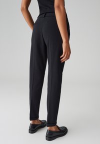 Pantaloni neri, sartoriali, con una texture liscia, design affusolato e orli risvoltati. Indossati con mocassini neri, dotati di tasche posteriori.