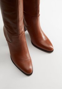 Bottes cuir marron à la cheville avec un bout pointu et un talon carré, présentant un design élégant et un détail de couture subtil.