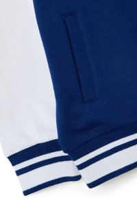 Suéter azul y blanco con puños acanalados en contraste. Presenta un diseño de rayas en blanco y azul marino en los puños. Tejido suave y texturizado.