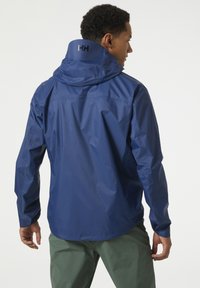 Marineblauwe lichtgewicht waterdichte jas met een capuchon, voorzien van een gladde textuur en logodetail bij de kraag. Verstelbare manchetten.