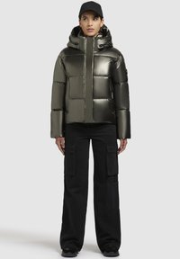 Dik, metallic olijfgroene jack met een capuchon, voorzien van een hoge kraag en stikseldetails. Gepaard met zwarte cargobroeken.