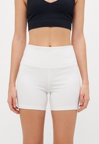 White athletic shorts with a high waistband, made of smooth, stretchy fabric. Features side pockets and a clean, minimalist design.