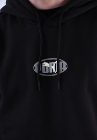 Sudadera negra de tejido suave con un gran logo ovalado que presenta una silueta y texto. Incluye cordones en la capucha.