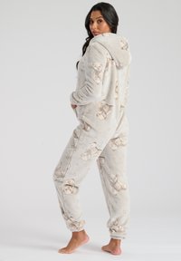 Lys grå hætteonesie lavet af blødt fleece-stof, med et stofmønster af teddy-bjørne og elastiske manchetter ved håndled og ankler.