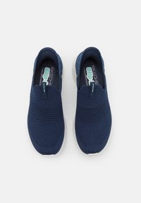 Navy blauwe instapsneakers van gebreid materiaal met een gestructureerde afwerking, voorzien van een witte zool en een treklus voor eenvoudig aan- en uittrekken.