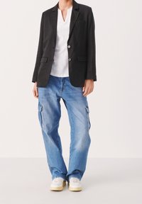 Schwarzer Blazer mit zwei Knöpfen, kombiniert mit einem weißen V-Ausschnitt-Shirt und hellblauen Cargo-Jeans mit Seitentaschen. Weiße Sneakers runden den Look ab.