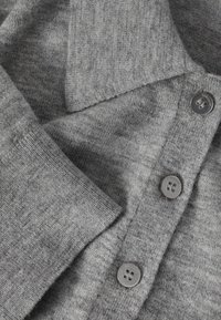 Pull gris en tricot avec un col en V, présentant une texture lisse et trois boutons gris sur la patte de boutonnage. Les manches pliées sont visibles.