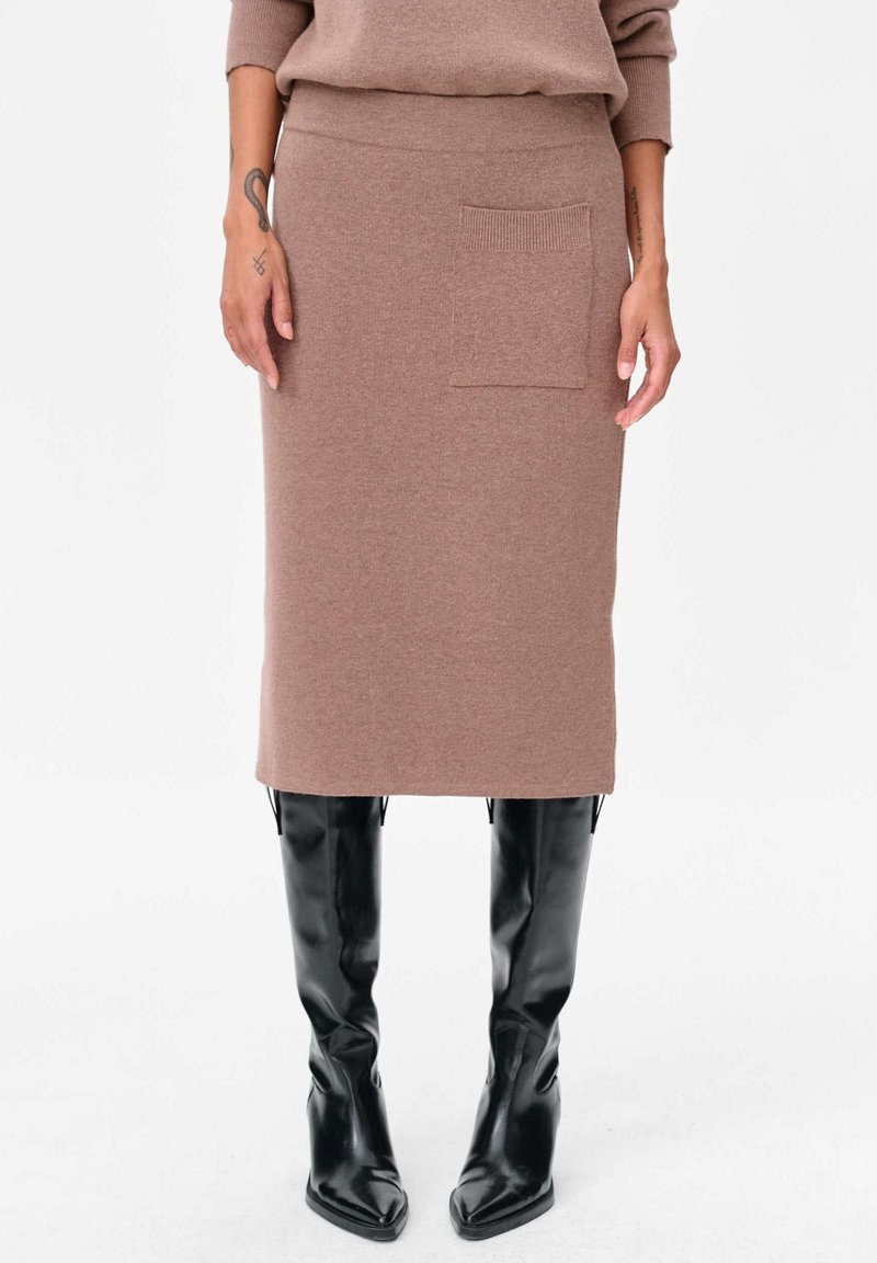 Brede, mid-length bruine rok van gebreid materiaal met een textured tailleband en een voorzak, gecombineerd met zwarte kniehoge laarzen. Gladde stofafwerking.