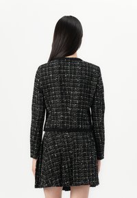 Schwarz-weißer Tweed-Jacke mit Rundhalsausschnitt und langen Ärmeln, kombiniert mit einem passenden, ausgestellten Rock. Strukturierter, texturierter Stoff.