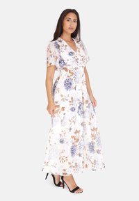 Blomster maxi kjole i hvid med blå og brune blomster. Har en v-udskæring, korte ærmer og en tætsiddende talje. Bæres med sorte hæle.
