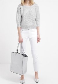 Jersey gris de punto, pantalones blancos ajustados, zapatos metálicos plateados, llevando una bolsa de tote texturizada en gris con acentos negros y correas dobles para el hombro.