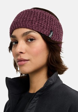 Knit, maroon headband featuring a textured pattern and a logo patch. Worn with a black fleece jacket. Close-up view of the wearer’s face.