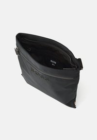 Borsa in nylon nero con chiusura a zip, logo impresso e rivestimento interno morbido. Design elegante e rettangolare con una singola tasca frontale.