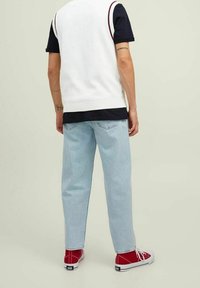 Weißer ärmelloser Strickpullover über einem marineblauen T-Shirt, kombiniert mit hellblauen, lässig sitzenden Jeans und roten Sneakers mit weißen Sohlen.