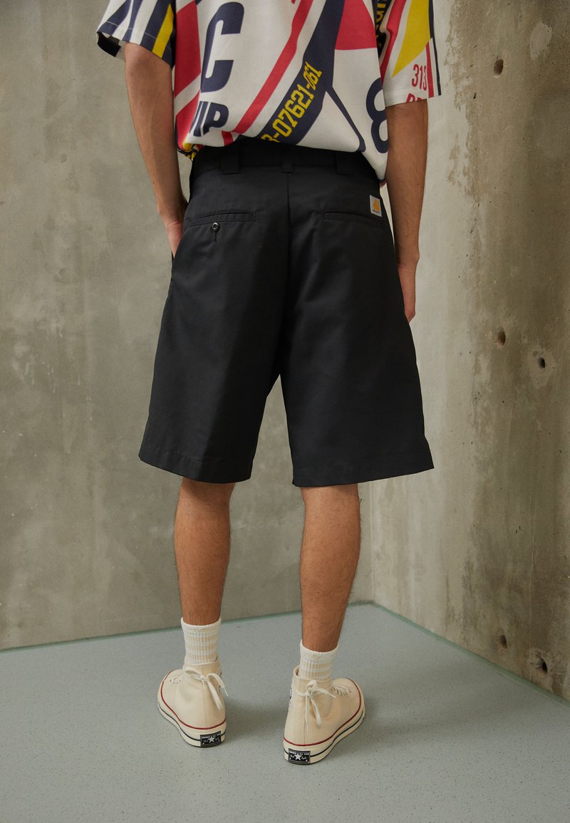 Sorte knælange shorts med en glat tekstur, to baglommer, parret med beige sko og hvide ribbede sokker.