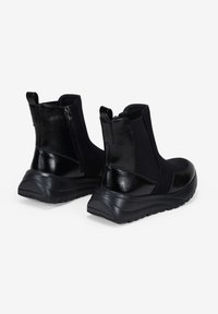 Bottines noires avec un dos en cuir verni lisse, des côtés en tissu texturé et une semelle en caoutchouc épaisse avec un léger talon.