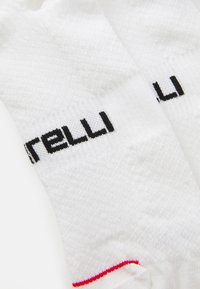 Valkoiset urheilupersonal socksit, joissa on teksturoitu muotoilu, musta "Pirelli" -brändäys ja punainen yksityiskohta yläreunassa.