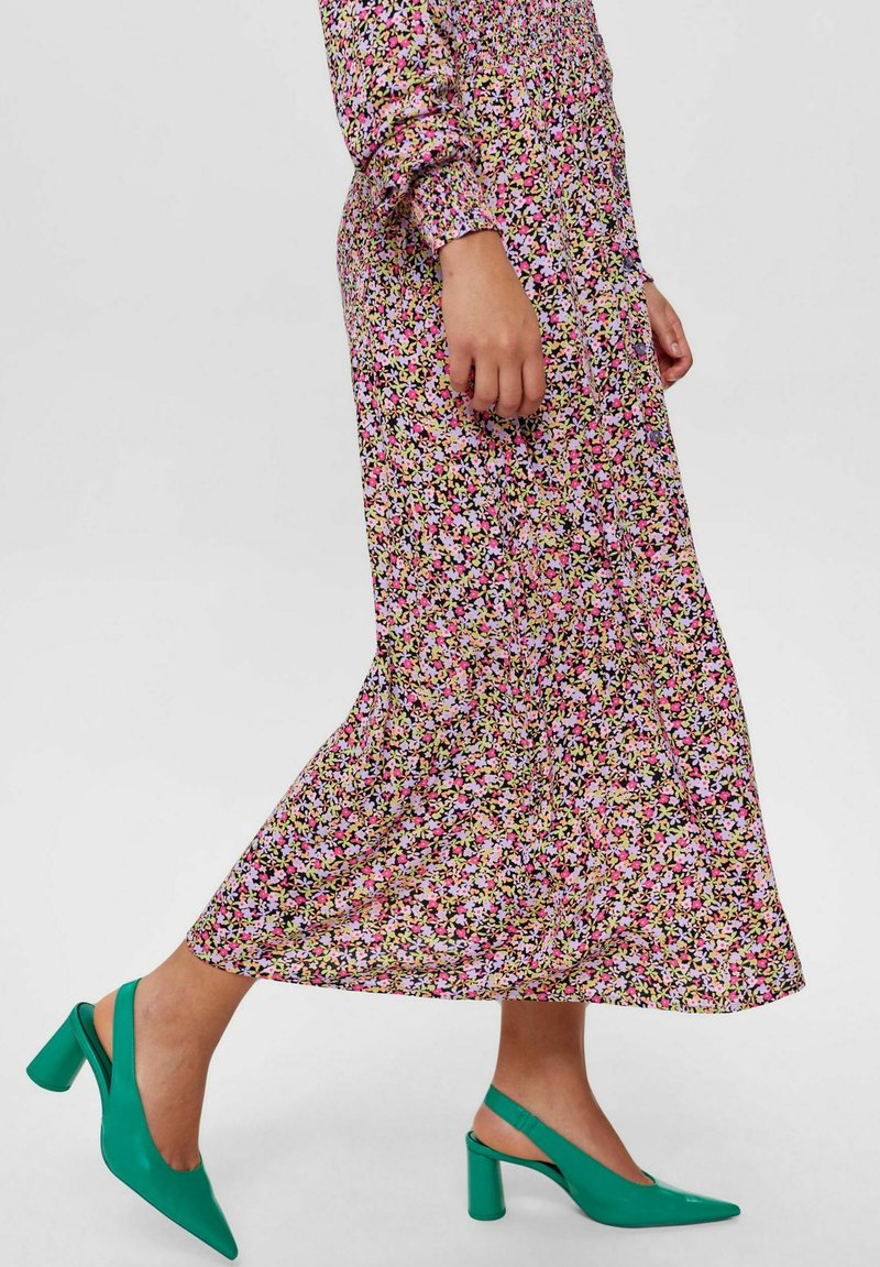 Kwiatowa sukienka maxi na czarnym tle, ozdobiona różowymi, żółtymi i białymi wzorami; zestawiona z zielonymi butami na obcasie w stylu slingback.