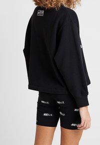 Black oversized sweatshirt with a small logo on the back, paired with black shorts featuring white "NIKE AIR" text and a fitted design.