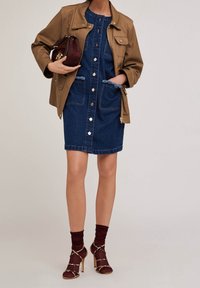 Brown jacket over a blue denim dress with buttons and pockets. Strappy heels with a maroon sock. Metallic hardware accents.