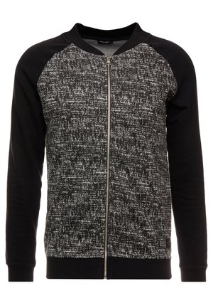 Sort og grå mønstret lynlåstrøje med ensfarvede sorte ærmer, ribstrikkede manchetter og rund halsudskæring.