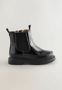 Stivale alla caviglia nero lucido con suola in gomma spessa, pannelli laterali elastici e foderatura interna marrone morbida su uno sfondo neutro.