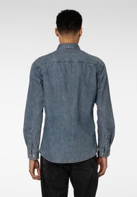 Denimskjorte i en lys blå nyanse med lange ermer, knappede mansjetter og klassisk krage. Har bakskjøt og subtile sømdetaljer.