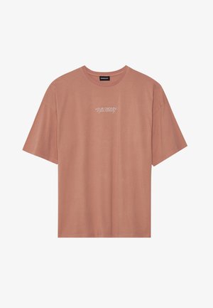 T-shirt à manches courtes, rose pâle, en coton doux. Avec un col rond et du texte blanc : "VOTRE ÉNERGIE est votre monnaie" sur le devant.