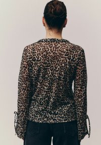 Prozirna bluzica s leopard uzorkom i dugim rukavima, sa trakama za vezanje na manžetama. Tkanina ima glatku teksturu i suptilan sjaj.