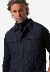 Quiltad marinblå väst med dragkedja, ståkrage och två framfickor. Har en texturerad yta och en avspänd passform.