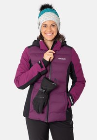 Lila und schwarze Steppjacke mit Reißverschluss, Kapuze und Logo; schwarze Handschuhe befestigt. Strickmütze mit blauen und weißen Akzenten und einem Pompon.