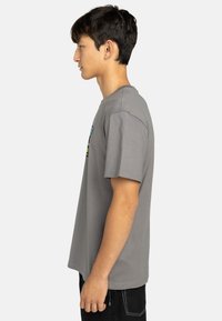 Graues Baumwoll-T-Shirt mit kurzen Ärmeln, Rundhalsausschnitt, seitlichen Nähten und einem bunten Grafikdruck auf der Vorderseite, kombiniert mit schwarzen Jeans.