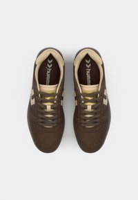 Sneakers in camoscio marrone con dettagli in tan, caratterizzati da una punta tonda, lacci piatti e il logo "hummel" sulla linguetta e sui lati.