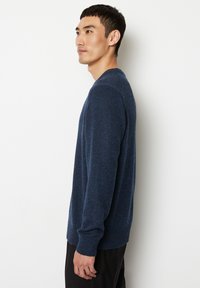 Gestreifter navyblauer Pullover mit Rundhalsausschnitt, gerippten Bündchen und Saum, der subtile Einsprenkelungen in hellblau für Textur und visuelles Interesse aufweist.