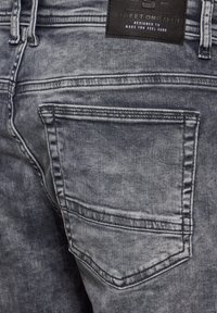 Jeans de denim gris con un acabado texturizado, que presentan un diseño de bolsillo trasero, costuras en contraste y una etiqueta de cuero negro en la cintura.