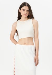 Top corto beige acanalado combinado con una falda blanca que presenta acentos laterales a cuadros naranjas, textura suave y diseño ajustado.