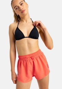 Schwarzer, dreieckiger Bikini-Oberteil kombiniert mit leuchtend korallenfarbenen Badeshorts, die über einen elastischen Bund und einen Kordelzug, eine glatte Textur und seitliche Taschen verfügen.