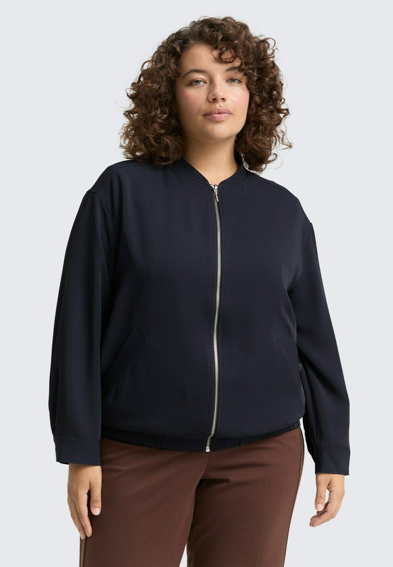 Veste de bombardier marine avec fermeture éclair à l'avant, col côtelé, poches latérales et coupe décontractée ; présente une texture lisse et un ourlet légèrement élastique.