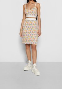 Kaksiosainen, värikäs asuste, jossa on monivärinen ruutukuosi; lyhyt toppi ohuilla hihnoilla, tiukka midi-hame, yhdistettynä paksupohjaisiin valkoisiin lenkkareihin.