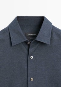 Donkerblauw katoenen overhemd met knoopsluiting, brede kraag en zichtbaar merkembleem aan de binnenkant van de halslijn.