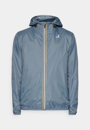 Veste légère grise imperméable avec capuche, dotée d'une fermeture éclair à l'avant avec une bande jaune et rouge, et d'un logo sur la poitrine.
