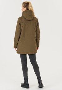 Olivgrön jacka med huva, långa ärmar och rak skärning. Har ett mjukt tyg och en enkel design, bärs över svarta skinny jeans och ankelstövlar.