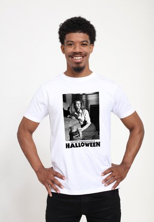 Weißes Baumwoll-T-Shirt mit einer schwarz-weißen Grafik einer sitzenden Frau, darunter der Text "JOHN CARPENTER’S HALLOWEEN".