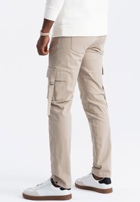 Béžové cargo kalhoty se postranními kapsami, lehce zúženou nohavicí a jemnými švy. Nosené s bílými teniskami.