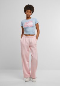 Lyseblå cropped t-shirt med pink tekstgrafik, parret med pink sweatpants med elastisk talje og opsmøgede kanter. Hvide sneakers.